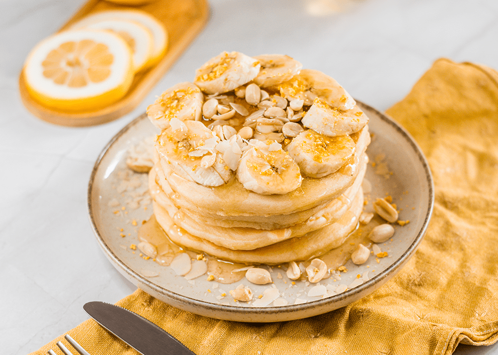 Stack of protein pancakes topped with banana on a gold edged plate